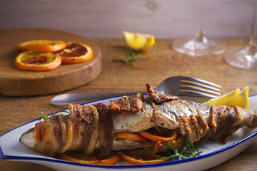 Grilled bacon-wrapped fish with oranges and rosemary, served with lemons - Image