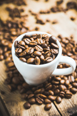 Coffee beans in white cup on the rustic wooden background. Selective focus. Shallow depth of field.