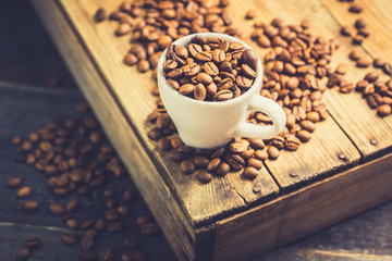 Coffee beans in white cup on the rustic wooden background. Selective focus. Shallow depth of field.