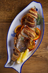 Grilled bacon-wrapped fish with oranges and rosemary, served with lemons - Image