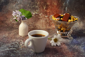 Morning coffee in a hurry: a cup of coffee, flowers in a vase, dried fruits and sweets in a vase, a burning candle.