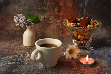 Obraz na płótnie Canvas Morning coffee in a hurry: a cup of coffee, flowers in a vase, dried fruits and sweets in a vase, a burning candle.