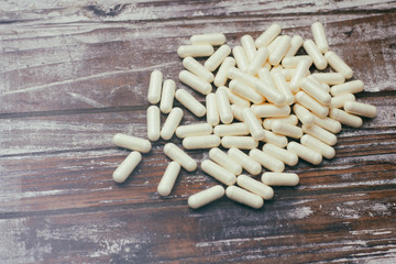 White capsules pills on old wooden table background. Medical concept.
