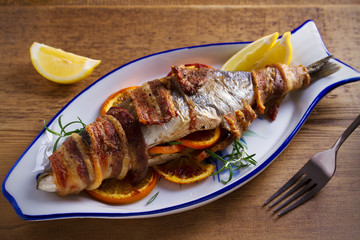 Grilled bacon-wrapped fish with oranges and rosemary, served with lemons - Image