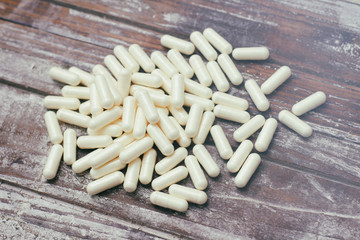White capsules pills on old wooden table background. Medical concept.