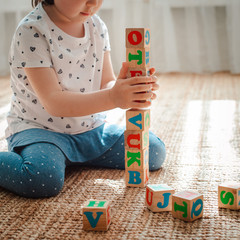 child plays with wooden blocks with letters on the floor in the room a little girl is building a...
