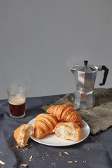 Continental breakfast with fresh croissant and natural coffee on a grey background.