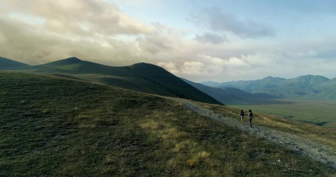 Aerial view flying above two people couple hiking or nordic walking outdoor on a trail path near Castelluccio di Norcia at sunset or sunrise.Approaching forward.Friends italian trip in Umbria.4k drone