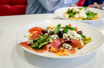 Delicious Italian pasta in a plate on a white table in a restaurant. Man in the background.