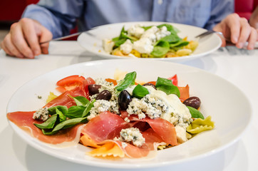 Tasty Italian pasta with vegetables and herbs in a plate on a white table in a restaurant. The man at the table eats pasta.