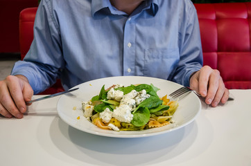Tasty Italian pasta with vegetables and herbs in a plate on a white table in a restaurant. The man at the table eats pasta.