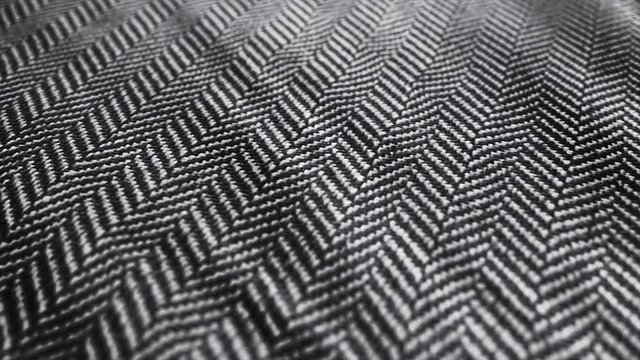 Herringbone fabric cloth close up background. Black and white tweed pattern, weaving, textile material is waving pan movement camera. 