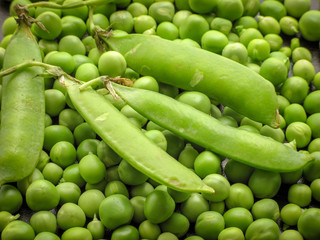 Closeup of fresh green peeled peas (Pisum sativum) and green peas in the pods on a wooden table