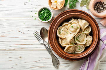 Traditional russian homemade meat dumplings pelmeni with butter and greens in ceramic bowl on white wooden table. Top view. Copy space.