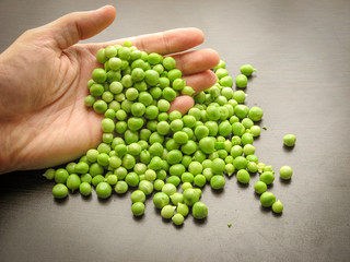 Close up of fresh green peeled peas in hand with brown wooden background.