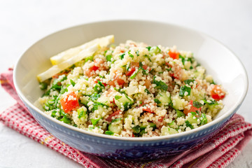 Traditional Arabic Salad Tabbouleh with couscous, vegetables and greens on concrete background. Selective focus.