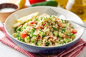 Traditional Arabic Salad Tabbouleh with couscous, vegetables and greens on concrete background. Selective focus.