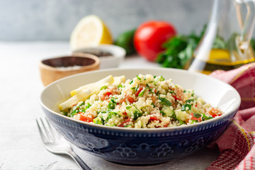 Traditional Arabic Salad Tabbouleh with couscous, vegetables and greens on concrete background. Selective focus.