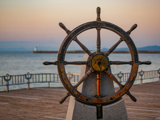 Captains steering wheel or rudder of an old wooden sailing ship in a port at sunset