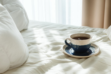 Bed with white sheets and pillow and cup of hot tea or coffee in the morning sun rays, selective focus