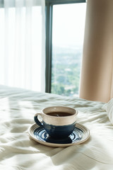 Bed with white sheets and pillow and cup of hot tea or coffee in the morning sun rays, selective focus