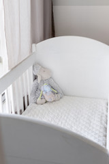 Cute children's cuddly toys decorating a white wooden crib, bedroom decor in neutral tones