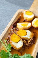 Boiled and Fried eggs in sweet and sour sauce with coriander in the wooden dish on table.