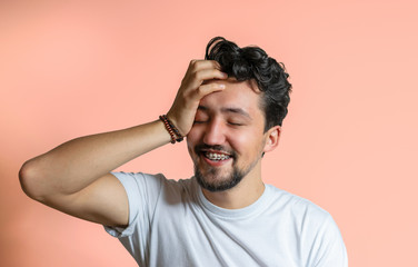 Portrait of a young man with braces smiling. A happy young man with braces on a pink background