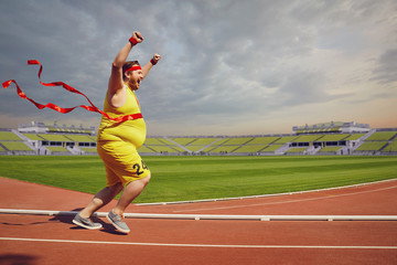 Fat funny man runs to the finish on track in the stadium.