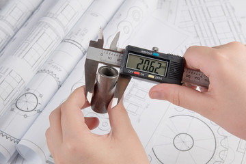 Engineer work. Measurement of the metal part with a caliper on the background of engineering...