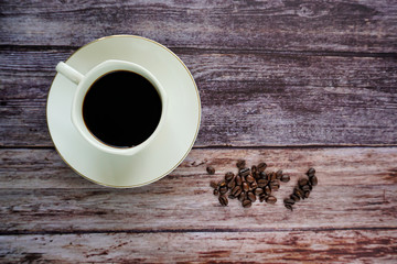 Cup of coffee and beans on a wooden textured background.