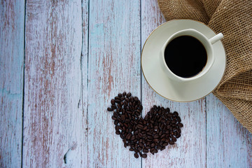 Cup of coffee and beans on a wooden textured background.