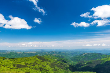 Panoramic view of idyllic mountain scenery with fresh green meadows and forests on a beautiful sunny day in springtime