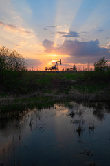 Equipment for oil and gas production works at sunset in the rays and glare of the sun next to the...