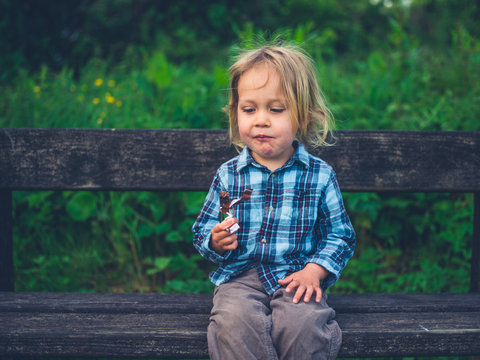 Little toddler eating a fruit bar on a bench