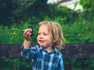Little toddler eating a fruit bar on a bench
