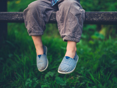 The feet of a toddler sitting on a bench in nature