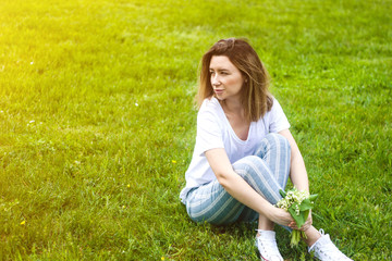 Stylish young woman sitting on green grass in sunny warm day