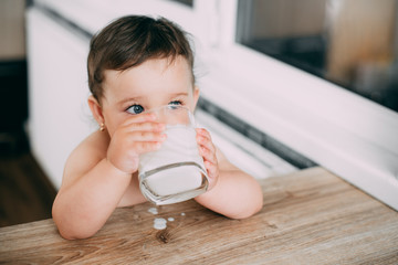 A little girl in the kitchen drinking milk or yogurt from a glass is very appetizing and greedy