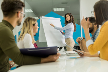 Obraz premium Confident young team leader giving a presentation to a group of young colleagues as they sit grouped by the flip chart in the office