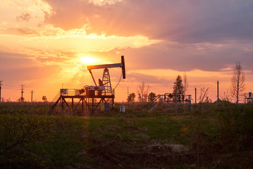 The equipment for oil and gas production works at sunset in the rays and glare of the sun. Oil well at sunset. Oil production with rocker at sunset. Rocking oil