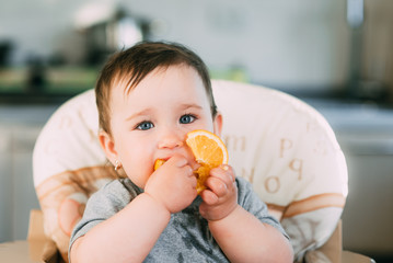 little girl sitting in baby chair, eating an orange