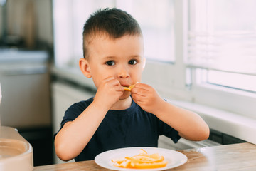 Beautiful Baby boy in the kitchen eagerly eating an orange, cut into wedges