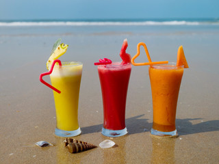 Three glasses of natural fruit juice with tubules on the seashore