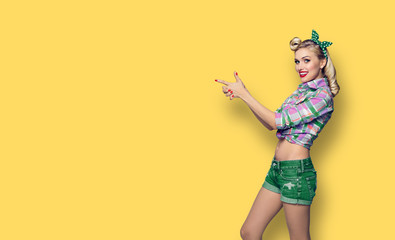 Photo of woman, dressed in pinup style, showing something or copyspace, over orange-yellow background