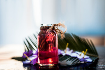 Rosemary concentration or essence in a glass bottle on wooden surface along with its flowers and some leaves.