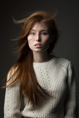 Attractive redhead model girl with long beautiful hair in the Studio on a gray background in a sweater of large knit, concept: beautiful hair color 