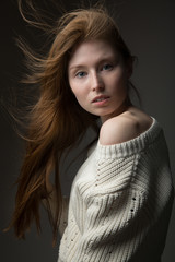 beautiful redhead model girl with long hair in the Studio on a gray background in a jacket of large knit