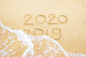 Happy new year. 2020 and 2019 written on the sand where 2019 is getting washed away by the wave