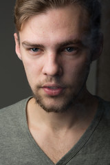Fototapeta premium Portrait of a young Caucasian Smoking man with a short beard and mustache on a dark background